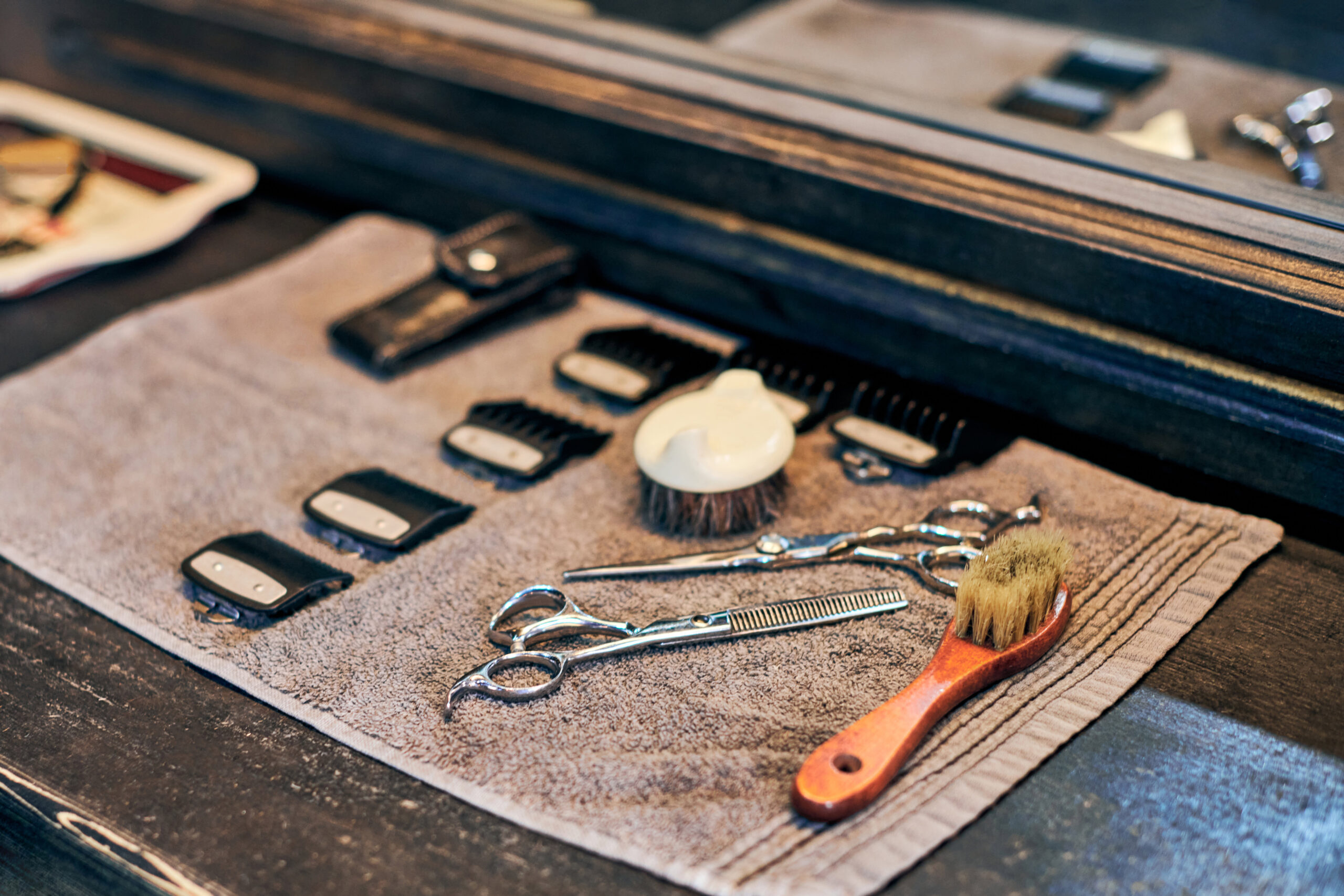 Barbershop haircut tools barber equipment on wooden countertop front of mirror, old vintage style interior. Hairdresser tools for stylish hair cut, clipper guide combs, scissors and hairbrushes